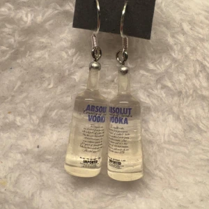 Örhängen med Absolut Vodka-flaskor - Unika örhängen formade som små Absolut Vodka-flaskor. Perfekt accessoar för dig som gillar roliga och annorlunda smycken. Hängande modell med silvriga krokar. Krokarna är i sterling silver 
