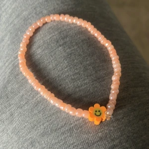 Rosa pärlarmband med blomma - Sött armband med små rosa pärlor och en gul blomma med smiley. Perfekt accessoar för att liva upp din outfit med en lekfull detalj.