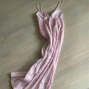 Rosa långklänning  - Rosa långklänning i glansigt tyg. Använd men fortfarande fin. Ca 34cm rakt över under bröstet men med stretchigt resår. 114cm under bröstet neråt. Har sytt om axelbanden, syns på bild. Typ M/L i storleken men passar även mig som har S