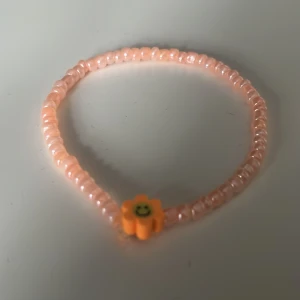 Pärlarmband med blomma - Sött armband med ljusrosa pärlor och en gul blomma med smiley. Perfekt accessoar för att liva upp din stil med en lekfull detalj.