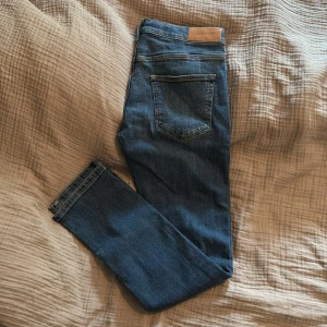 Blå jeans Gant med rak passform, oanvända  - Säljer ett par klassiska blå jeans med rak passform och femficksdesign. Jeansen har normal midja, längd fram 21cm, totallängd 82cm, midja 36cm. Ställbar midja. Helt oanvända, nypris 899kr