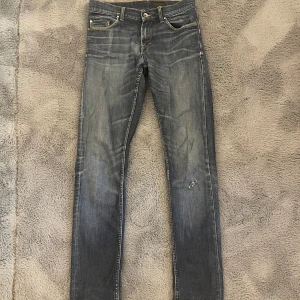 Slim jeans Tiger of Sweden  - Säljer ett par klassiska blå jeans (29:34)från Tiger of Sweden med snyggt slitna detaljer och raka ben. Gylf med dragkedja och knapp samt kontrastsömmar. Perfekta för en stilren och avslappnad look.