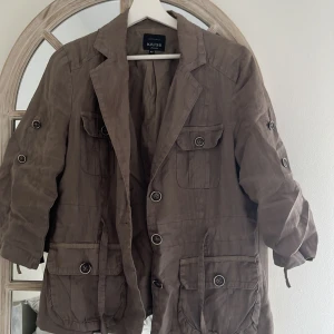 Brun kavajjacka från Kriss - Säljer en brun kavajjacka från Kriss med flera fickor och knappar framtill. Jackan har lång ärm med knappdetaljer och är tillverkad i ett lätt material som känns luftigt. Perfekt för dig som vill ha en stilren och praktisk jacka.