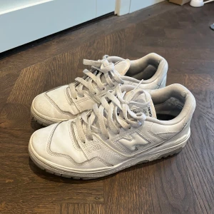 Vita New Balance 550 sneakers - Säljer ett par klassiska vita New Balance 550 sneakers med grå detaljer. Skorna har snörning, rund tå och platt sula. Perfekta för dig som gillar stilrena och sportiga sneakers med retrovibbar.