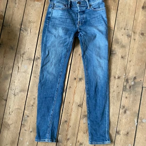 Blå jeans från Abercrombie & Fitch - Säljer ett par klassiska blå jeans från Abercrombie & Fitch med normal passform och raka ben. Jeansen har fem fickor, dragkedja och knapp framtill samt snygga kontrastsömmar. Perfekta till vardags och enkla att matcha.