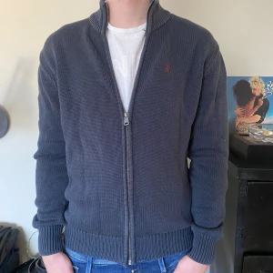 Stickad fullzip - Mörkblå stickad fullzip i bra skick, storlek m och han på bilden är 182.Har du frågor eller Funderingar kring plagget tveka då inte att höra av dig 