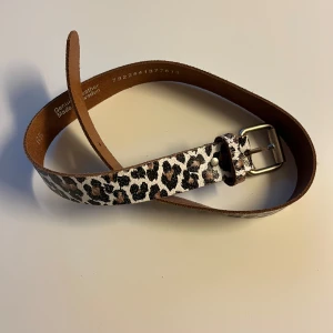 Leopardmönstrat bälte i skinn - Snyggt bälte i äkta skinn med leopardmönster och silverspänne. Bältet har en klassisk form och är tillverkat i Sverige. Perfekt accessoar för att lyfta din outfit med lite extra attityd. Lite slitet i strukturen men ska vara så!