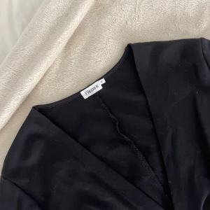 Svart omlottklänning från Filippa K - Säljer en svart omlottklänning från Filippa K med lång ärm och knytband i midjan. Klänningen har v-ringad hals och är tillverkad i ett mjukt, följsamt material.