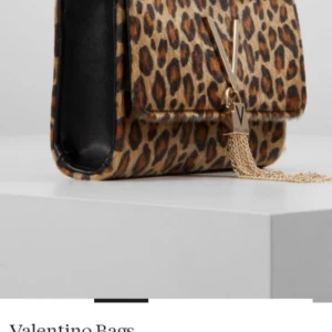 Leopardmönstrad axelväska från Valentino - Snygg axelväska från Valentino Bags i leopardmönster med guldfärgad V-detalj och kedja framtill. Väskan har ett fack med lock och magnetlås. Perfekt för att lyfta din outfit med lite extra attityd.