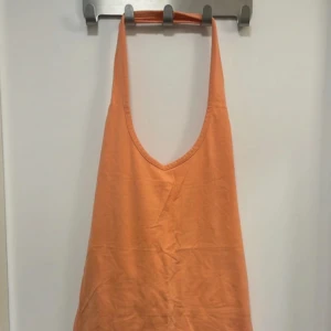 Persikofärgad ärmlös klänning - Säljer en enkel och snygg persikofärgad klänning med djup urringning och ärmlös design. Klänningen är i mjukt bomullsmaterial och har en rak passform som passar perfekt till sommaren.