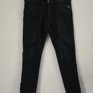 Svarta Replay Anbass jeans - Svarta jeans från Replay, modell Anbass. Klassisk femficksdesign med dragkedjegylf och smal passform. Byxorna har diskret Replay-logga vid fickan och är tillverkade i stretchigt material för extra komfort.