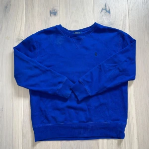 Blå sweatshirt från Polo Ralph Lauren - Säljer en blå sweatshirt från Polo Ralph Lauren. Den är lite kortare i modellen, extremt skön då den sitter lite lösare runt armarna. Ny pris runt 1200kr, mitt pris endast 299kr. Strl 10-12 år 150 cm. Om du har några funderingar är det bara att skriva.