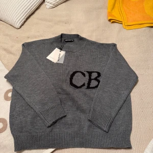 Grå stickad tröja från Cole Buxton - Säljer en grå stickad tröja från Cole Buxton med svarta initialer 'CB' på bröstet. Tröjan har rund halsringning och långa ärmar med ribbade muddar. Perfekt för en stilren och avslappnad look. Tröjan är aldrig använd bara testad och har tagsen kvar, pris kan diskuteras.