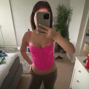 Rosa korsettopp med spetsdetaljer - Säljer en snygg rosa korsettopp med tunna axelband och spetsdetaljer. Toppen är croppad och har en figurnära passform som framhäver midjan. Perfekt för att lyfta vilken outfit som helst!