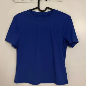 Blå t-shirt i syntetmaterial - En enkel blå t-shirt med rund hals och korta ärmar. Tillverkad i ett slätt syntetmaterial som känns mjukt mot huden. Perfekt för dig som gillar en klassisk och stilren look.