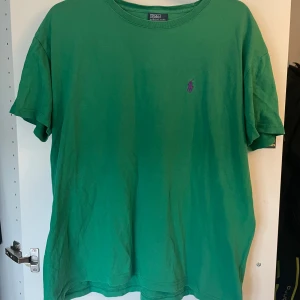 Grön t-shirt från Polo Ralph Lauren - Säljer en grön t-shirt från Polo Ralph Lauren med klassisk passform och lila broderad logga på bröstet. T-shirten är tillverkad i 100% bomull och har korta ärmar. 