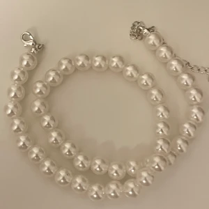  pärlhalsband - Säljer ett elegant halsband med vita pärlor och silverfärgat spänne. Perfekt för att ge en tidlös och stilren touch till din outfit. Halsbandet har rundade pärlor i jämn storlek och sitter snyggt runt halsen.
