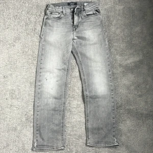 Grå straight legged jeans från Replay - Snygga grå jeans från Replay i modellen THAD. Jeansen har en slim passform och klassisk femficksdesign. De är tillverkade i denim och har diskreta slitningar för en trendig look. Perfekta till vardags för en stilren outfit. Fläck på framsidan