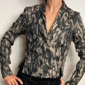 Mönstrad kavaj från Bitte Kai Rand - Säljer en snygg figursydd kort kavaj från den danska designerns Bitte Kai Rand i svart, khaki och beige med abstrakt mönster. Kavajen har klassisk krage, knäppning framtill och figurnära passform. Materialmix av polyamid, viskos och elastan. Mått: byst 44 cm axlar 38 cm, läng 47 cm