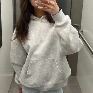 Grå hoodie med blå text - Säljer en ljusgrå hoodie med stor känguruficka och huva. På ryggen finns blå tryckt text . Oversize i modellen