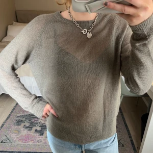 Grön stickad tröja - Säljer en enkel och stilren beige stickad tröja med rund halsringning. Tröjan har långa ärmar och är perfekt att matcha med jeans för en avslappnad look. Ganska genomskinlig! 