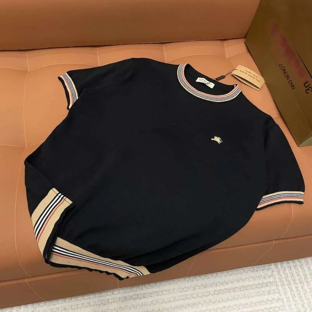 Svart t-shirt med klassiska Burberry-rutiga detaljer på ärmarna. Rund halsringning och diskret logga på bröstet. Perfekt för en stilren och trendig look.. T-paidat.