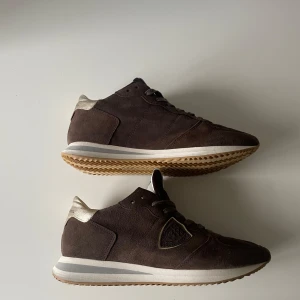 Bruna sneakers från Philippe Model - Snygga bruna sneakers från Philippe Model med ovandel i mocka och detaljer i beige. Helt nya har gått i dom nån gång inomhus. Nypris 3000kr. Box + dust bag och kort.