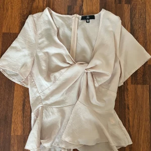 Ljusrosa omlottopp med volang - Säljer en ljusrosa omlottopp med korta ärmar och volang nertill. Toppen har en snygg twistad detalj framtill och är tillverkad i ett glansigt, mjukt material. Perfekt för dig som gillar feminina och trendiga plagg.