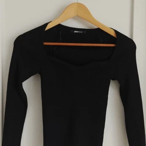 Svart långärmad topp från Gina Tricot - En svart långärmad topp från Gina Tricot med fyrkantig urringning. Toppen har en tight passform och är tillverkad i ett stretchigt material som sitter snyggt på kroppen. Perfekt att styla med jeans eller kjol.