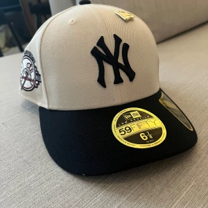 New Era Yankees 59FIFTY keps - Snygg 59FIFTY keps från New Era med New York Yankees-logga framtill och 100th Anniversary brodyr på sidan. Kepsen är beige med blå skärm och detaljer, tillverkad i bomull. Perfekt för dig som gillar sportig stil.