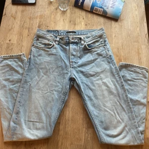 Ljusblå jeans från Nudie Jeans - Säljer ett par ljusblå jeans från Nudie Jeans med klassisk femficksdesign och snygga kontrastsömmar. Byxorna har normal passform och raka ben. Perfekta för dig som gillar en stilren och tidlös look.