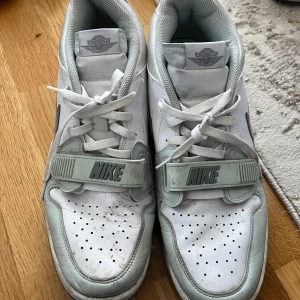 Nike Air Jordan sneakers i vitt och grått - Säljer ett par Nike Air Jordan sneakers i vitt och ljusgrått med klassisk snörning och bred kardborre över foten. Skorna har perforerad tå, grå swoosh och Air Jordan-logga på hälen. Perfekta för dig som gillar streetwear och sportig stil. Har köpt de för 1400kr men säljer de för endast 700kr ( vid snabb köp kan priset diskuteras)