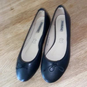 Svarta ballerinaskor - Säljer ett par klassiska svarta ballerinaskor. Skorna har rund tå och en liten söt rosett framtill. Perfekta för dig som vill ha en stilren och tidlös sko till vardags. Köpta från Sellpy och har ingen tecken på användning. 