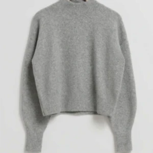 Grå stickad tröja från & Other Stories - Mysig grå stickad tröja från & Other Stories med hög, ribbad hals och långa ärmar med ribbad armsmudd. Tröjan har en rak och något loose passform. Lite nopprig