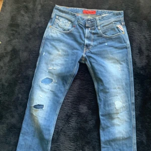 Anbass replay jeans  - Säljer ett par blå jeansbyxor från Replay   Stl 31/34 med slitningar,  normal passform. Snygga detaljer och tydliga slitningar för en trendig look.