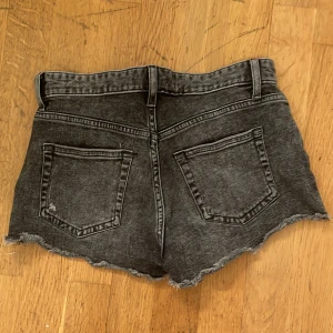 Svarta jeans shorts - Snygga svarta jeansshorts med rå, fransig kant och klassisk femficksdesign. Shortsen har hög midja och en slitning framtill för en cool look. Perfekta för sommaren och passar till allt.