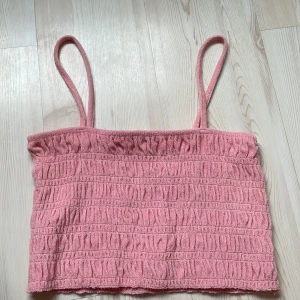 Rosa smockad linnetopp från H&M - Supersöt rosa linnetopp från H&M med smala axelband och smockad struktur. Toppen är croppad och gjord i mjuk frotté som känns skön mot huden. Perfekt för varma dagar när du vill ha en chill och trendig look.