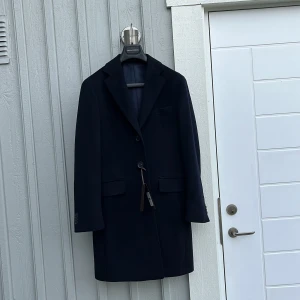 Mörkblå rock från Oscar Jacobson - Stilren mörkblå rock från Oscar Jacobson. I storlek 46 vilket motsvarar S/M. Ny pris är 5500kr. Mitt pris 2890kr. Den är oanvänd och lappar sitter kvar. Hör av dig vid minsta lilla fundering eller fråga! 