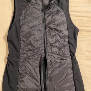 Svart dunväst med dragkedja - Snygg svart dunväst med quiltad framsida och dragkedja. Västen har en sportig look med släta sidor och praktiska fickor. Perfekt för lager-på-lager och passar till många olika outfits.