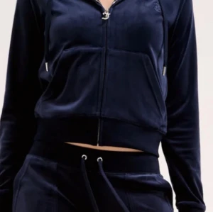 Juicy cotoure Mörkblå velour hoodiejacka - Mörkblå hoodiejacka i mjuk velour med dragkedja framtill och snörning i huvan. Jackan är croppad och har en stor ficka framtill. Perfekt för en chill och sportig look.