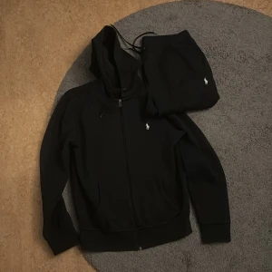 Svart Ralph Lauren dress - Svart hoodie från Ralph Lauren med dragkedja och huva. Tillsammans med matchade byxor. Inga defekter. Väldigt snygg dress men har växt ut den. STRL TRÖJA- S STRL BYXA- M. Pris kan diskuteras 