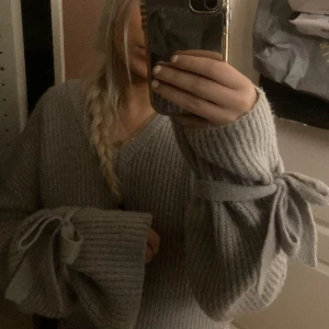 Grå stickad tröja NA-KD x Linn Ahlborg🎀 - Supermysig grå stickad tröja med v-ringning från NA-KD x Linn Ahlborg. Tröjan har långa ärmar och en söt rosettdetalj vid ärmslutet🎀