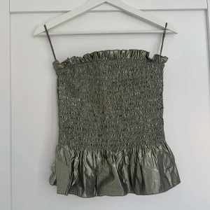 Glittrig grå linnetopp från & Other Stories - Supersnygg glittrig grå linnetopp från & Other Stories med smockad struktur och volangkant nertill. Tunt axelbandslinne med metallic finish som verkligen sticker ut. Perfekt för dig som vill ha något extra till outfiten!