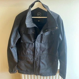 Mörkblå fieldjacka från Five Seasons - Mörkblå fieldjacka från Five Seasons med klassisk krage, fyra stora fickor framtill och dragkedja med tryckknappar🔥. Jackan har en stilren look och är tillverkad i slitstark polyester. Perfekt för dig som gillar enkel och funktionell stil till höst, vår och vinter 🍂. Jackan har även justerbara remmar på insidan så man kan justera passformen! Skriv till mig om eventuella frågor och priset kan självklart diskuteras vid snabb affär!✅ 