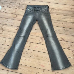 Grå bootcut jeans Cheap Monday 26/30 - Snygga grå bootcut jeans från Cheap Monday i modellen Booty. Jeansen har en cool tvätt med ljusare partier och klassisk femficksdesign. Materialet är en mix av bomull, polyester och elastan för skön stretch och passform.