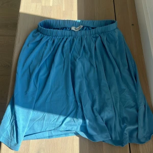 Blå kortkjol från MSCH - Supersöt blå kortkjol från MSCH med resår i midjan och lätt, flowigt tyg. Perfekt för varma dagar när du vill ha en chill och avslappnad look. Kjolen har en enkel design utan mönster och är riktigt skön att bära.