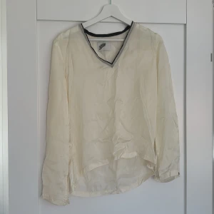 Krämvit blus i silke från Stay Dirty - Säljer en krämvit blus i 100% silke från Stay Dirty. Blusen har v-ringning med svart kant, lång ärm och något längre bakstycke. Perfekt för dig som gillar en clean men ändå unik look.