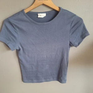 Blå croppad topp från Gina Tricot XS - Enkel och stilren blå croppad topp från Gina Tricot, med rund halsringning och korta ärmar. Tillverkad i mjuk bomull som känns skön mot huden. Perfekt att matcha med jeans eller kjol för en avslappnad look.
