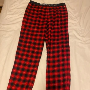 Rödrutiga byxor Tommy Hilfiger - Snygga rödrutiga byxor från Tommy Hilfiger med svart resår i midjan och logga. Mjukt material och klassiskt rutmönster i rött och svart. Perfekta för chill dagar hemma eller när du vill ha en avslappnad look.
