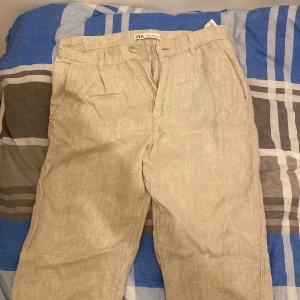 Beiga linnebyxor från Zara, strl 36 - Snygga beiga linnebyxor från Zara i storlek 36. Byxorna har raka ben, bälteshällor och sidfickor fram samt passpoalfickor bak. Perfekta för en chill och stilren look under varmare dagar.